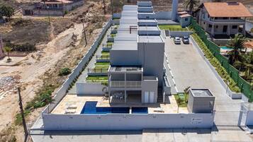 Un edificio moderno con piscina en la azotea, varios balcones y una cerca verde.