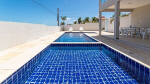Ein Swimmingpool mit zwei weißen Liegestühlen, einem Tisch mit Stühlen und Blick auf den Himmel und Palmen.