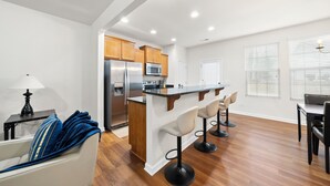 Een moderne keuken met houten kastjes, een roestvrijstalen koelkast en een inbouwmagnetron. Er is een bar met twee barkrukken en een eettafel met stoelen.