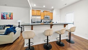 Een moderne keuken met houten kastjes, een roestvrijstalen koelkast en een magnetron. Er is een bar met krukken en een eettafel.