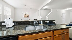 Een moderne keuken met granieten werkbladen, een roestvrijstalen spoelbak, houten kastjes en een kroonluchter.