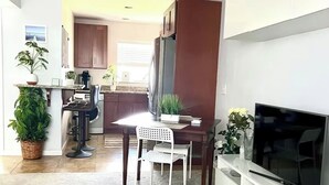 Une cuisine moderne avec des meubles en bois foncé, un coin repas avec une chaise blanche et un téléviseur à écran plat posé sur un meuble blanc.