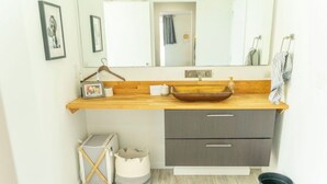 A bathroom with a wooden vanity, a large mirror, and a small trash bin. - Home Base for World Cup (Kansas City)