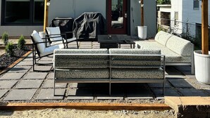 A modern patio area with outdoor furniture, a string of lights, and a view of a white building. - Home Base for World Cup (Kansas City)