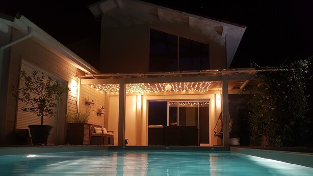 Ein Schwimmbad mit überdachter Terrasse, Sitzgelegenheit und einer Topfpflanze.