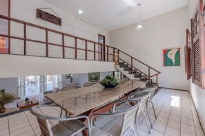 Un comedor amplio con una mesa larga y sillas de mimbre, una escalera y vistas del patio exterior.