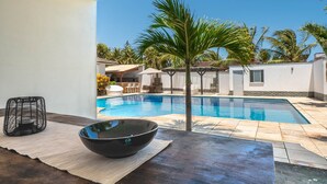 A modern poolside area with a clear view of a swimming pool, palm trees, and a dining area with outdoor furniture. - Casa Com Piscina em Porto das Dunas by Carpediem (Aquiraz)
