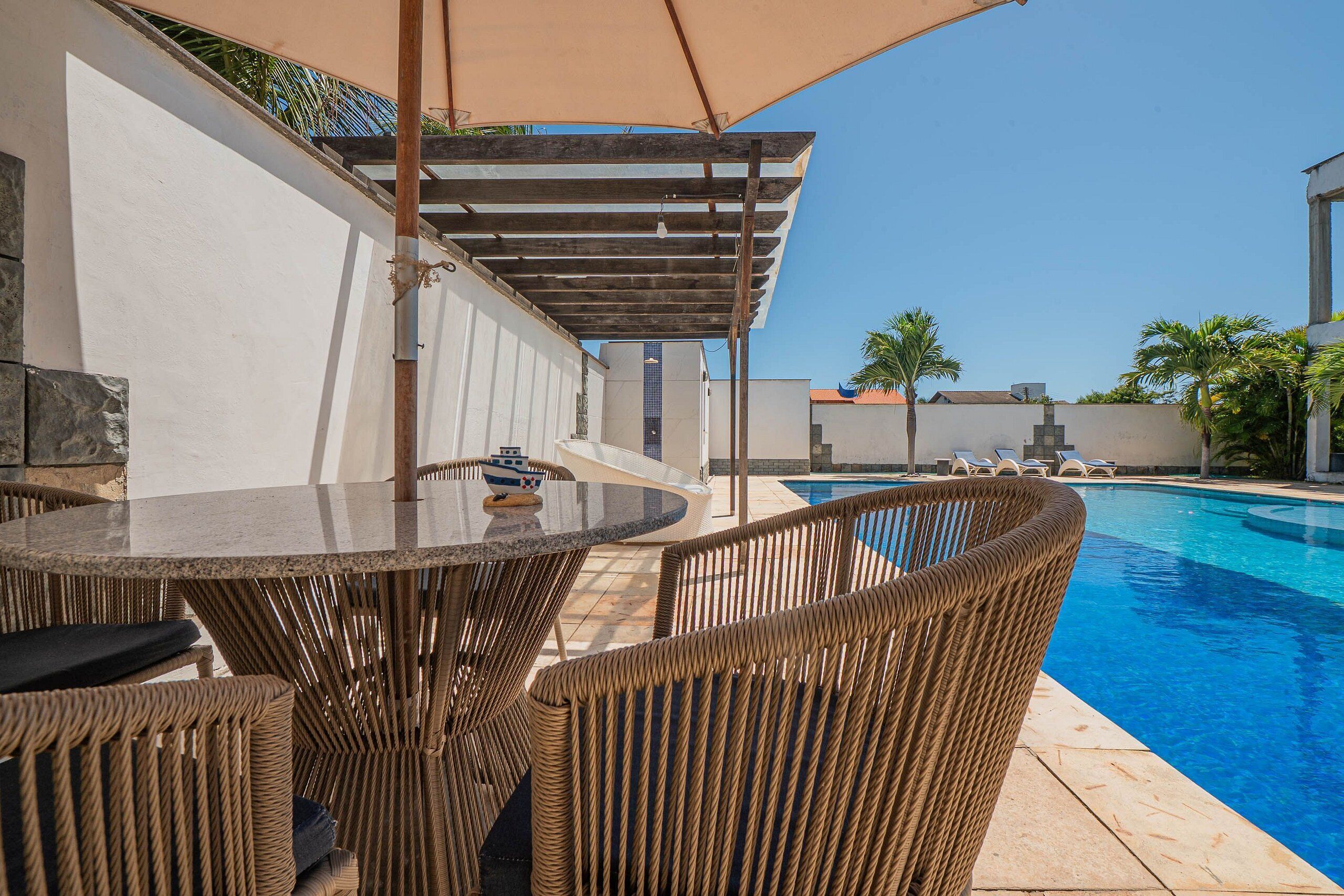 Ein Poolbereich mit Korbmöbeln, einer Pergola und einem kühlen, blauen Pool.