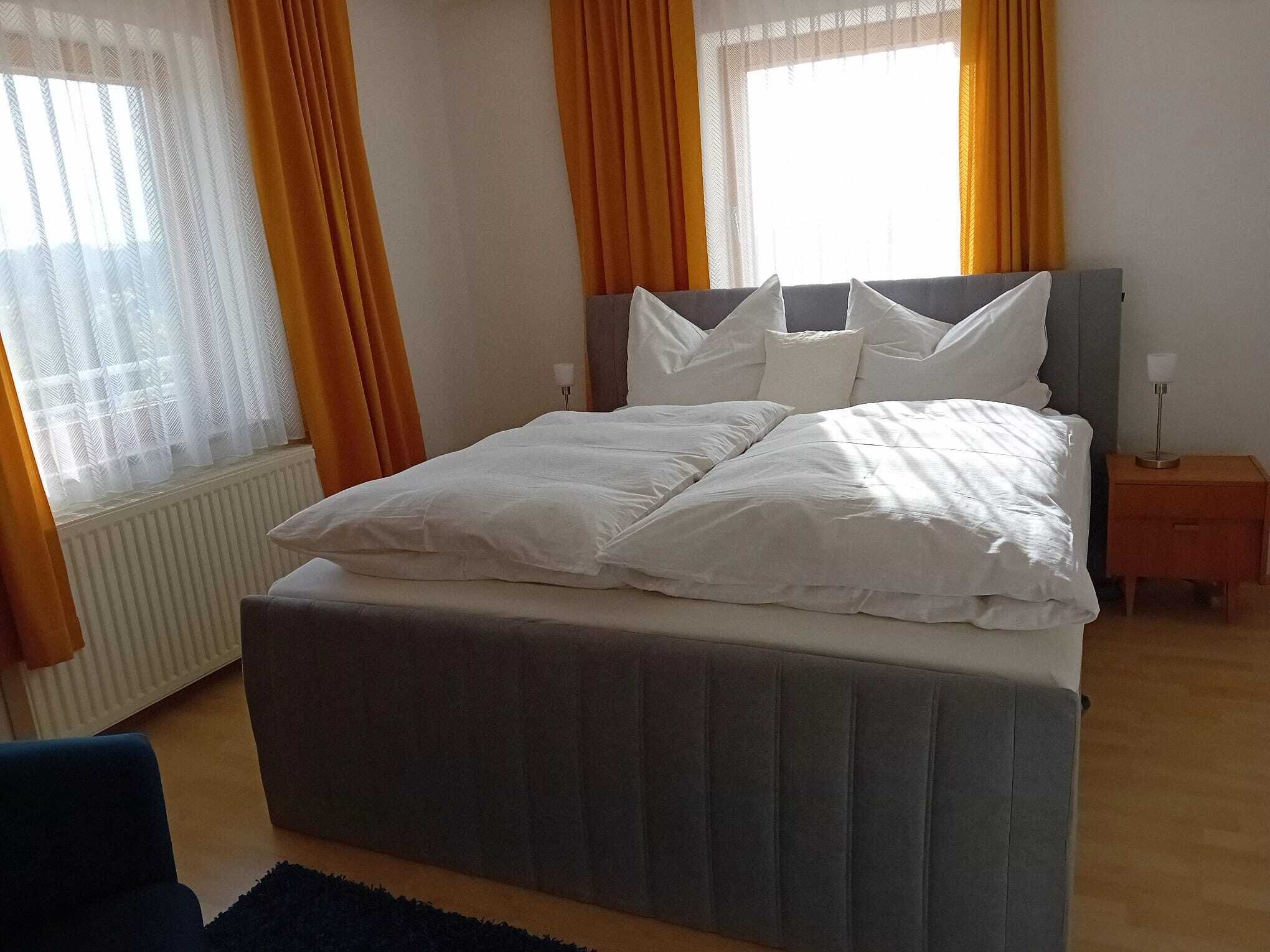 Een slaapkamer met een groot bed, een nachtkastje en een raam met gordijnen.