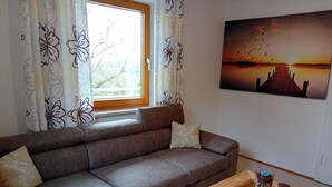 A living room with a sofa, a coffee table, and a painting of a sunset. - Vacation home to feel good in, great pool to relax in, Donaucard included! (Engelhartszell)