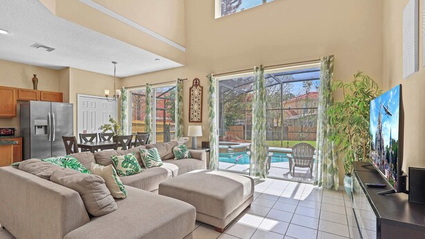 A spacious living area with a large sofa, a dining table, and a view of a swimming pool. - Mins 2 Disney Adventure Villa 8BR, VR & Theater (Kissimmee)