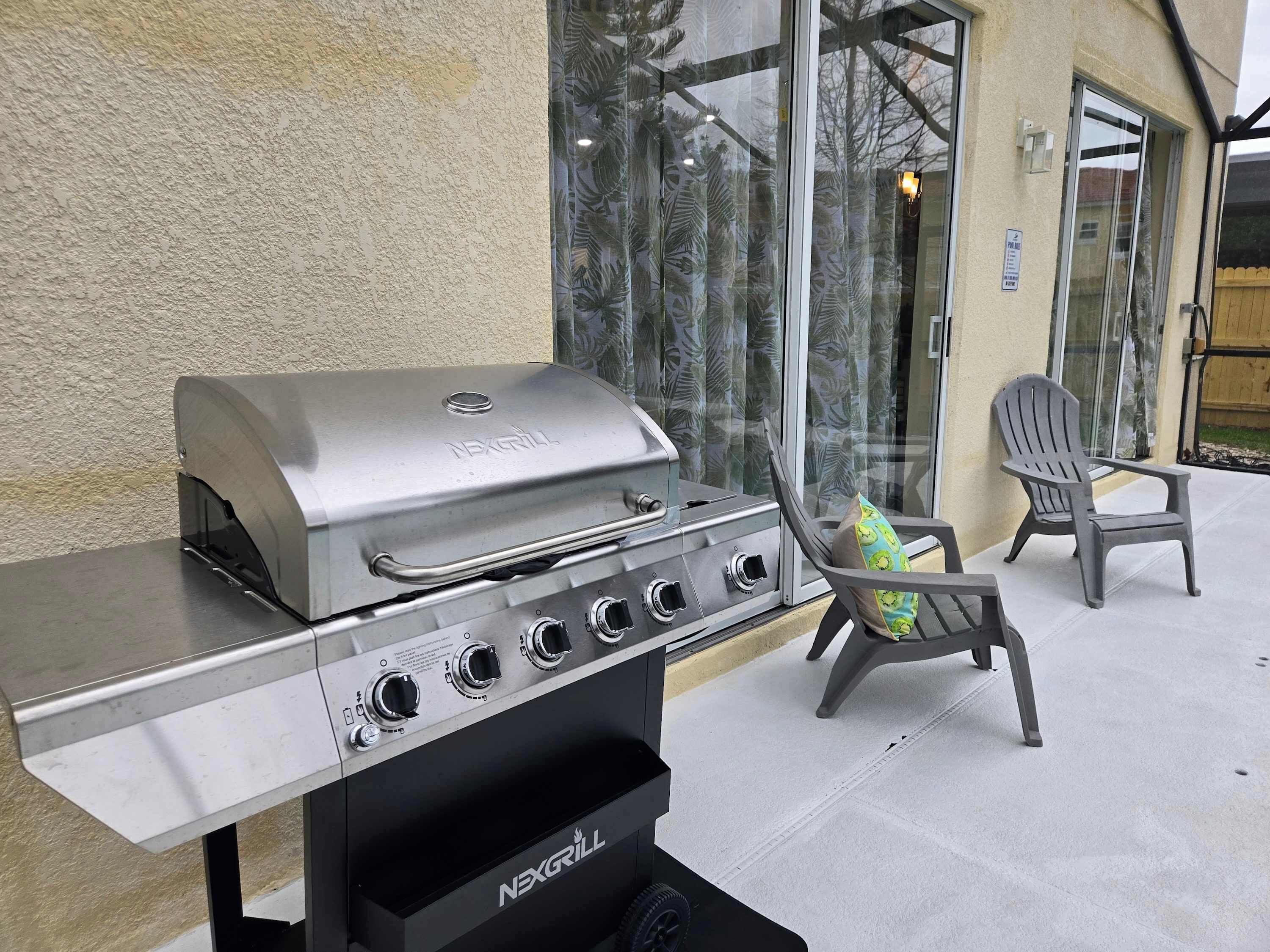 A NEXGRILL barbecue grill with four burners, a side shelf, and a chimney. There are two Adirondack chairs and a glass door leading to a patio.