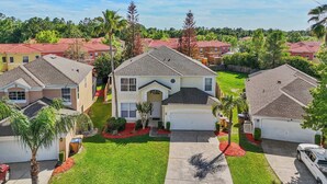 A residential neighborhood with houses featuring red-tiled roofs, well-maintained lawns, and a central driveway. - Mins 2 Disney Adventure Villa 8BR, VR & Theater (Kissimmee)