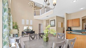 A dining area with a wooden table and chairs, a chandelier, and a kitchen in the background. - Mins 2 Disney Adventure Villa 8BR, VR & Theater (Kissimmee)