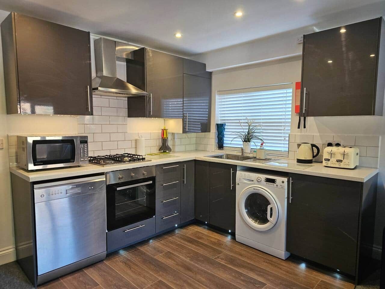 A modern kitchen with stainless steel appliances, a dishwasher, a washing machine, and a microwave.