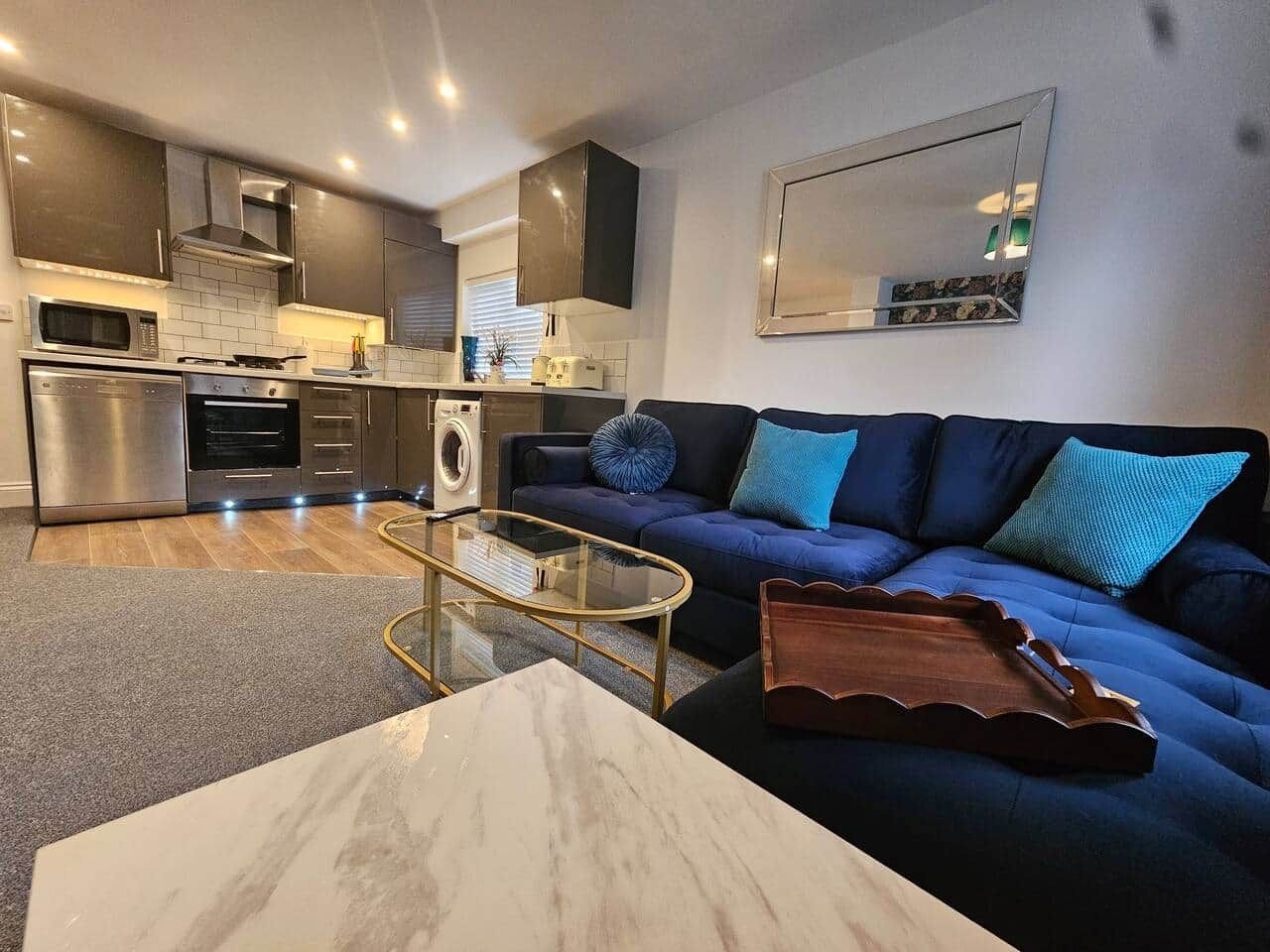 Una sala de estar moderna con sofá, mesa de centro y zona de cocina al fondo.
