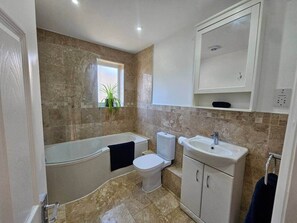 Un baño con bañera, inodoro, lavamanos y ventana.