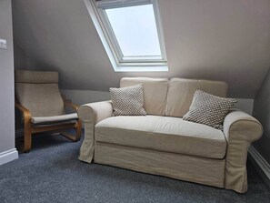 A room with a beige sofa, a wooden chair, and a skylight. - Stay Zen Apartments- luxury central parking garden (Woking)