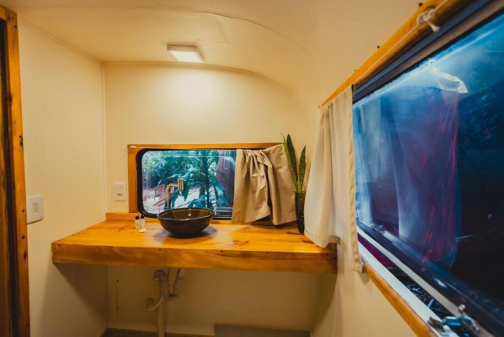 A compact kitchen with a wooden countertop, a window with curtains, and a view of greenery outside.
