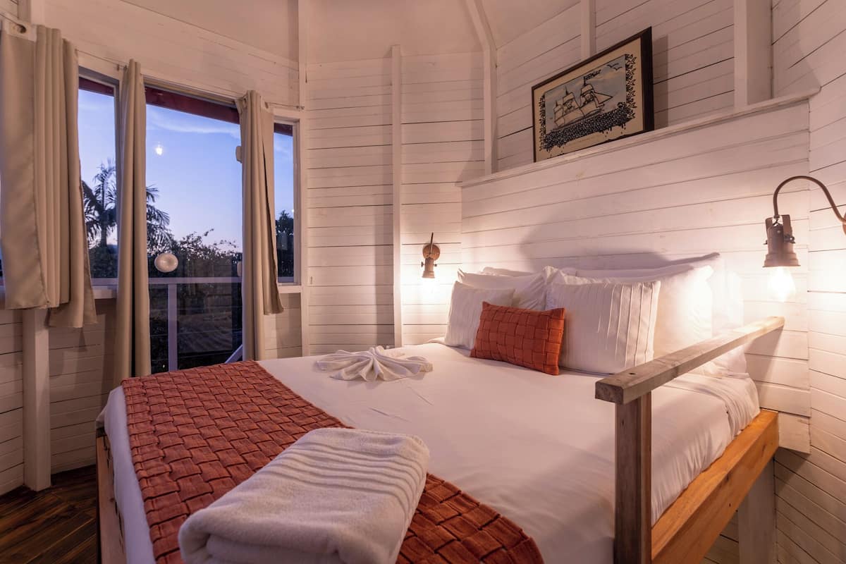 Ein Schlafzimmer mit einem hölzernen Bett, weißen Bettwäsche, einer rot-weißen Karodecke, einem Holz-Kopfteil und einem gerahmten Bild an der Wand.