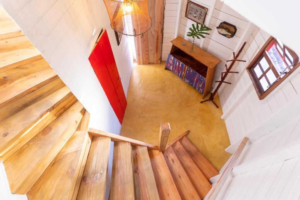A wooden staircase leading to a room with a red door, a wooden bench, and a window with white shutters.