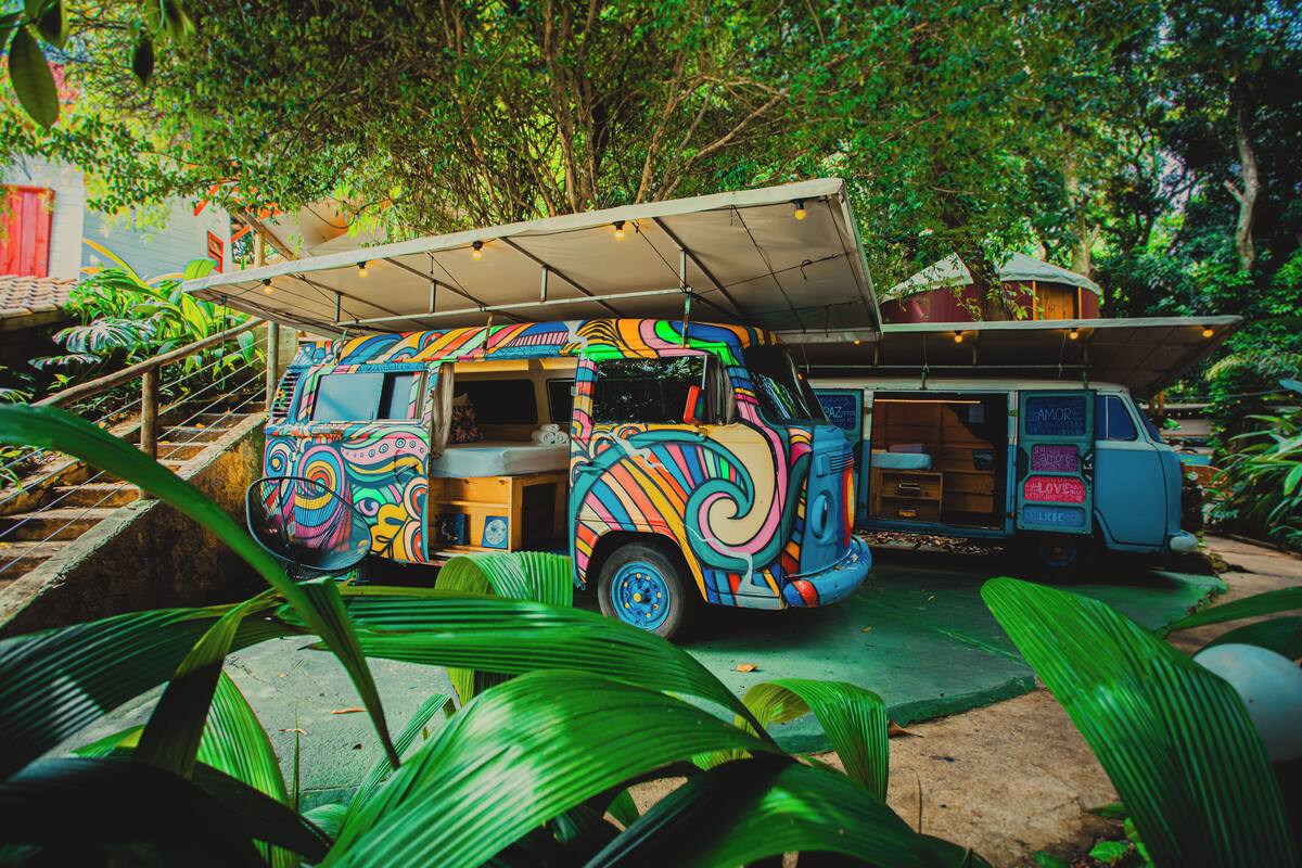 Ein farbenfroher Food-Truck parkt in einem üppigen Garten mit überdachter Sitzgelegenheit.