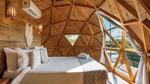 Een gezellig slaapkamer met een puntdak, een groot bed, houten wanden en uitzicht op groen.