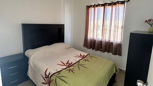 Quarto com cama, mesa de cabeceira, guarda-roupa e janela com cortinas.