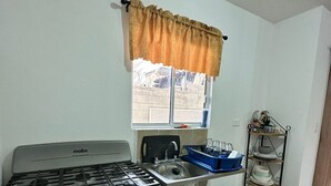 Uma cozinha com fogão, pia, janela e prateleiras.