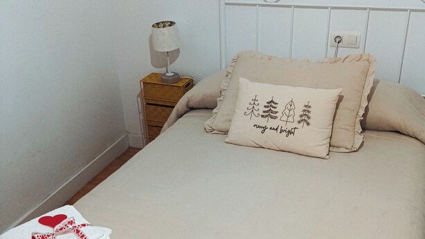 Un lit bien fait, recouvert d’une couvre-lit beige, avec deux oreillers et deux serviettes pliées, décorées de motifs en forme de cœur.