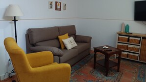Un salon avec un canapé marron, un fauteuil jaune, un tapis à motifs et une petite table en bois.