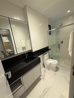 A modern bathroom with a black countertop, a white toilet, and a glass-enclosed shower. - HOTEL JD VILLAGE  (Itapema)