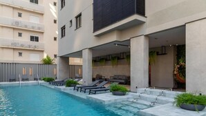 Una piscina interior moderna con sillones de descanso y macetas, rodeada por un edificio de diseño minimalista y una zona de estar cubierta.