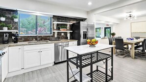 Una cocina moderna con armarios blancos, un refrigerador de acero inoxidable y una zona de comedor con mesa y sillas.