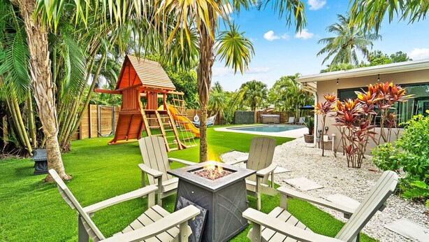 Un patio trasero con un parque infantil de madera, un brasero y una piscina.