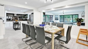 Una cocina moderna con armarios blancos, un comedor con mesa y sillas de madera, y un ventanal con vistas al verdor.