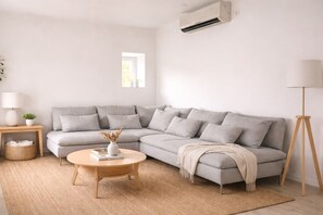 Un salon moderne avec un canapé d’angle gris, une table basse ronde en bois, un lampadaire et un climatiseur fixé au mur.