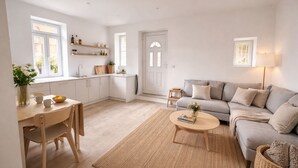Et moderne interiør med et køkken, spiseområde og opholdsstue, med hvide skabe, en grå sofa og et lille sofabord.