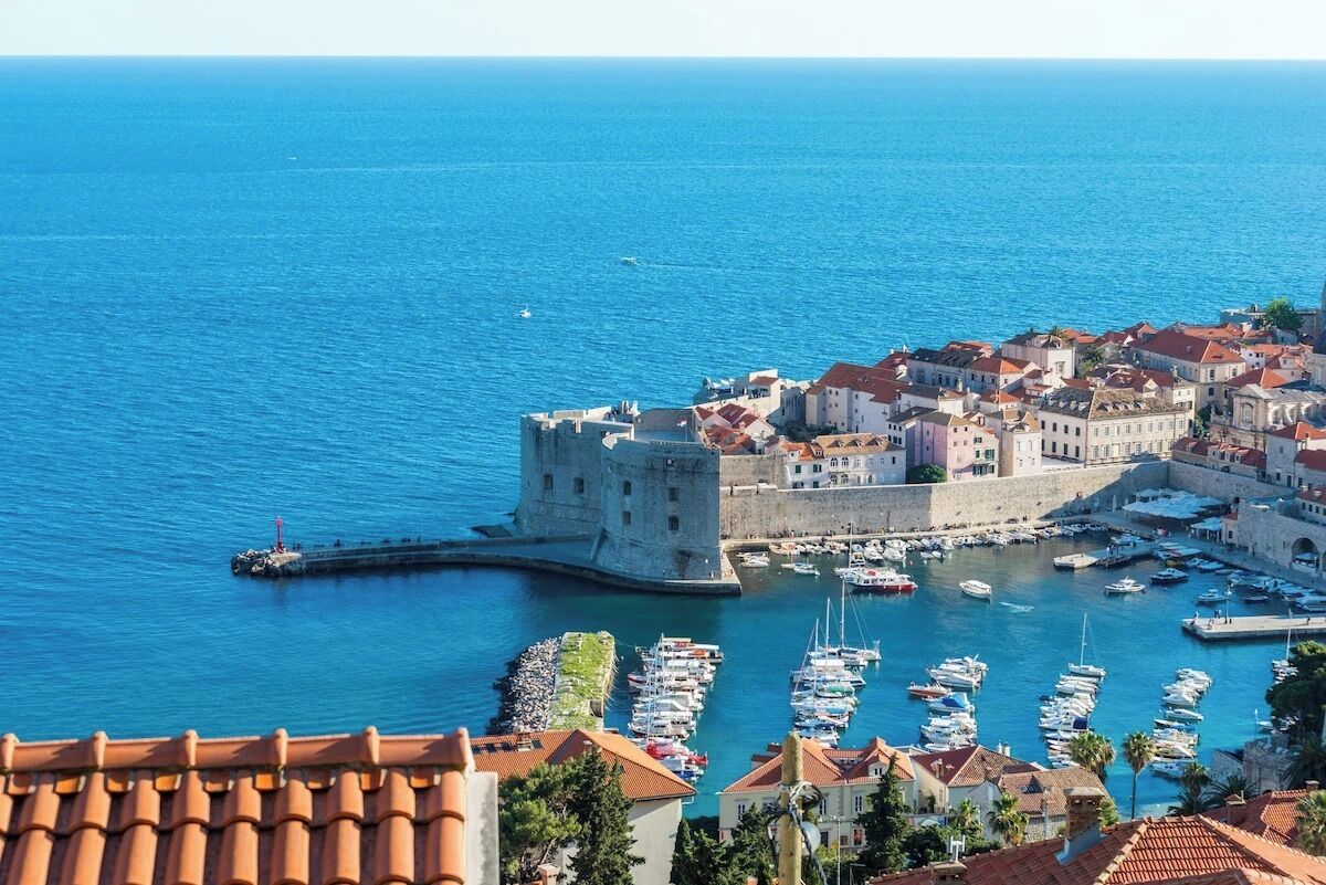 A coastal town with a historic fort, a marina with boats, and traditional buildings.