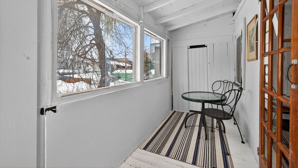 A small, enclosed porch with a single table and chairs, a door, and a window overlooking a tree and buildings. - Cozy & practical apartment in Hull 5 min to Ottawa (Gatineau)