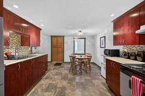A compact kitchen with wooden cabinets, a dining table with chairs, a stove, and a microwave.