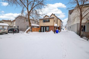 A residential street with houses, parked cars, and snow-covered ground.