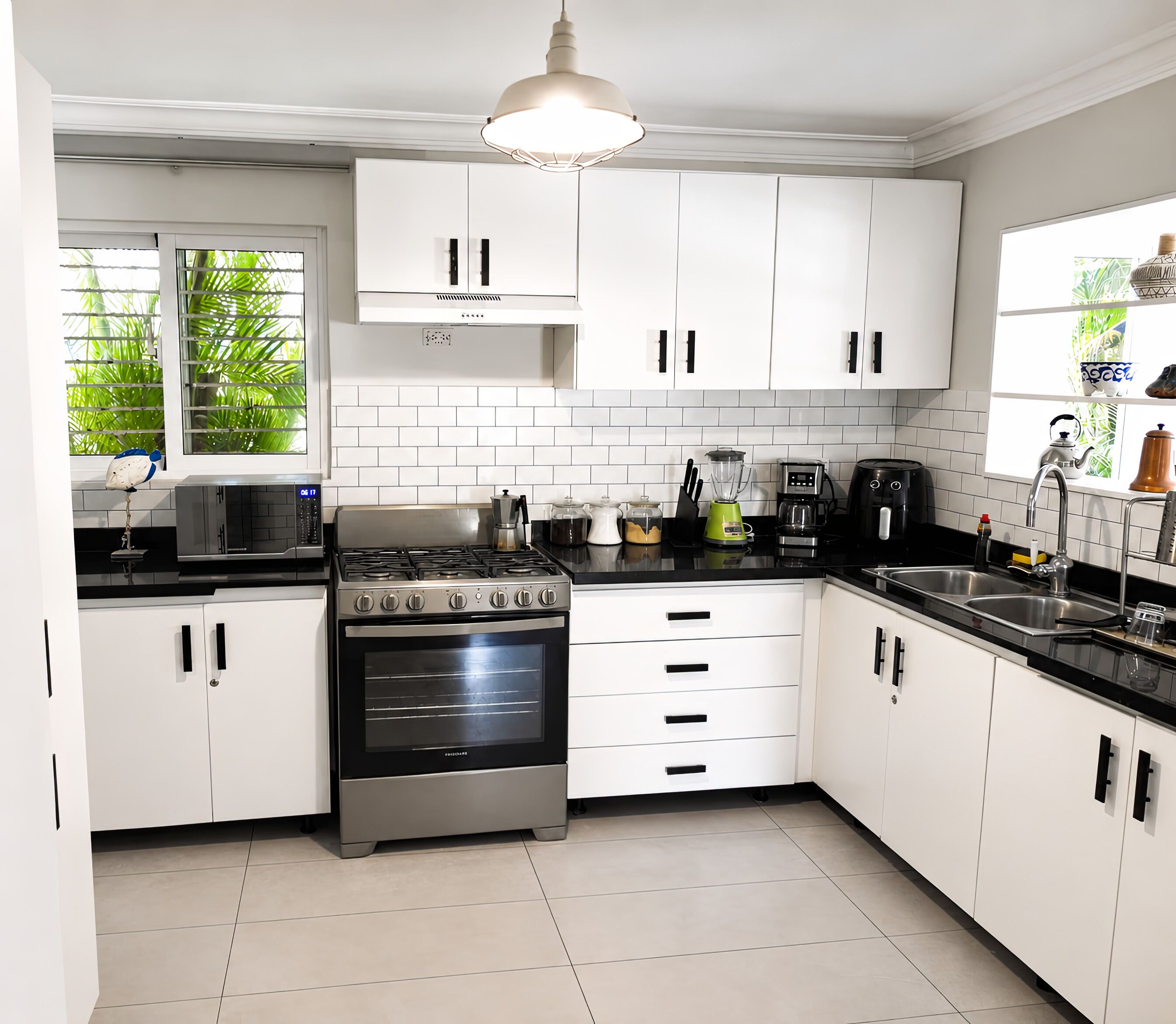 Une cuisine moderne avec des meubles blancs, une cuisinière en acier inoxydable, un four encastré, une machine à café et une bouilloire.