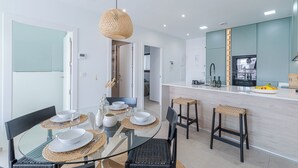 Una cocina moderna con una isla central, un área de comedor con mesas de vidrio y un espacio de sala con un sofá.