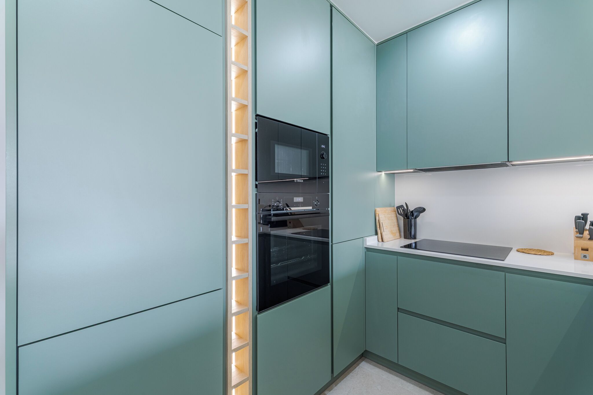 A modern kitchen with teal cabinetry, a black microwave, and a built-in oven.