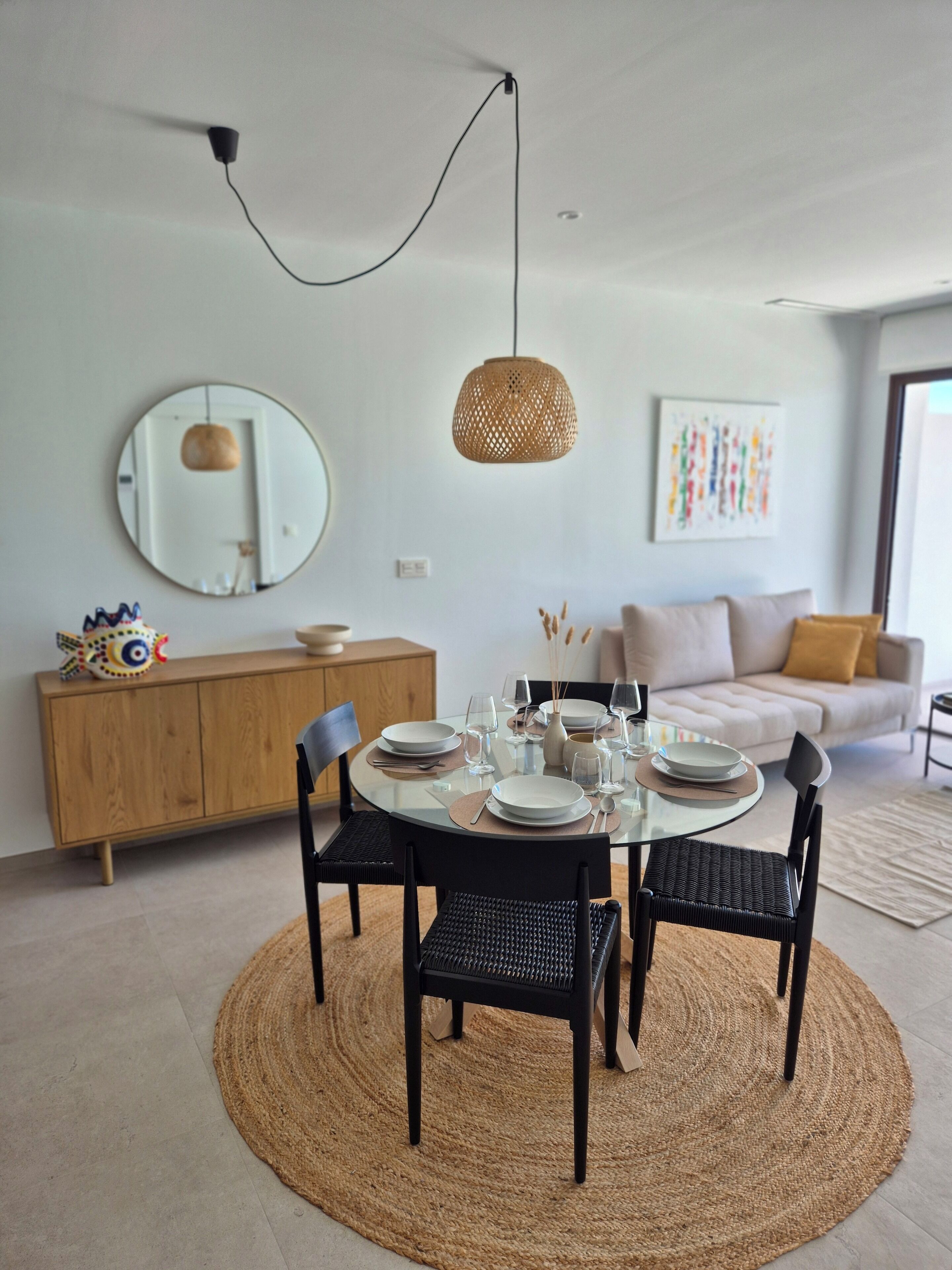 A dining area with a round table set for four, surrounded by black chairs, a woven rug, and a hanging light fixture.