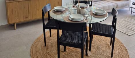 A dining area with a round table set for four, surrounded by black chairs, a woven rug, and a hanging light fixture.