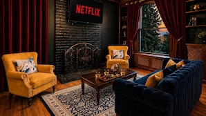 Ein Wohnzimmer mit Kamin, einer Couch, Sesseln, einem Couchtisch und einem Fernseher, der 'NETFLIX' anzeigt.