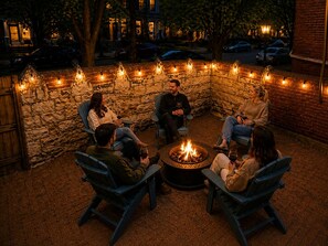 Eine Gruppe von Menschen sitzt um eine Feuerstelle in einer Außenpatio-Terrasse mit Steinmauern und Lichterketten.