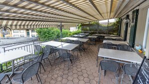 An outdoor patio with hexagonal tiles, metal tables and chairs, and a striped awning providing shade. - Gasthof Sternen Thörishaus (Neuenegg)
